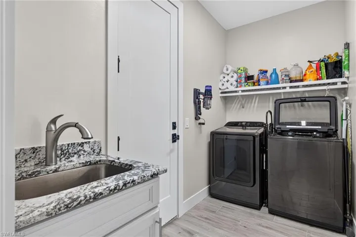 Utility room featuring a utility sink, a speckled countertop, light cabinetry, and wood-finish flooring