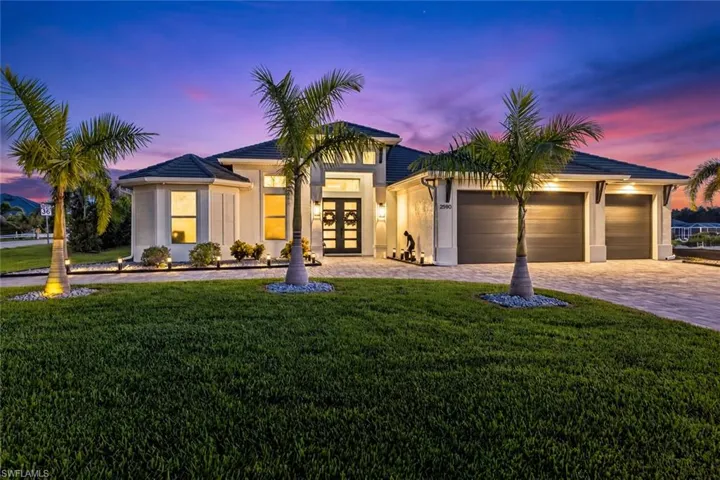 Stucco exterior with a tiled roof, paver driveway, three-car garage, and established landscaping
