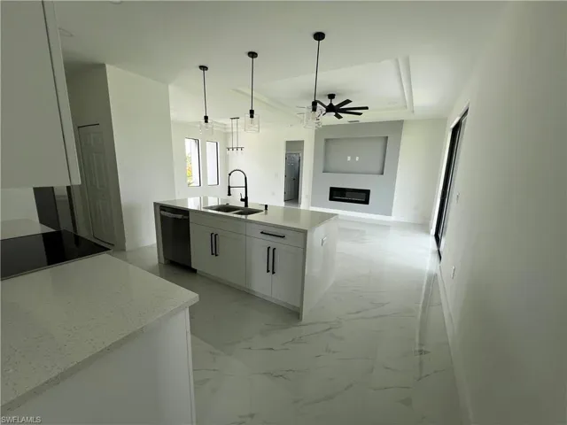 Kitchen with light tile patterned floors, white cabinets, ceiling fan, sink, and dishwashing machine