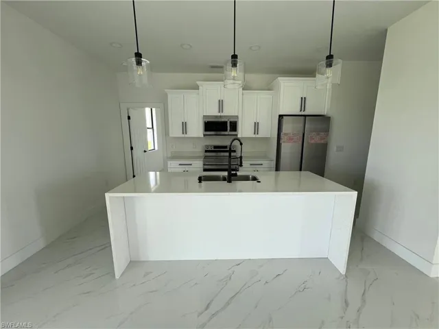 Kitchen featuring stainless steel appliances, light tile patterned floors, a kitchen island with sink, sink, and white cabinetry