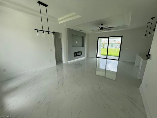 Unfurnished living room with a tray ceiling, light tile patterned floors, and ceiling fan