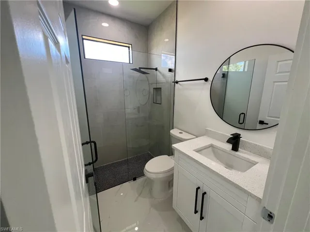 Bathroom with a shower with door, toilet, vanity, and plenty of natural light
