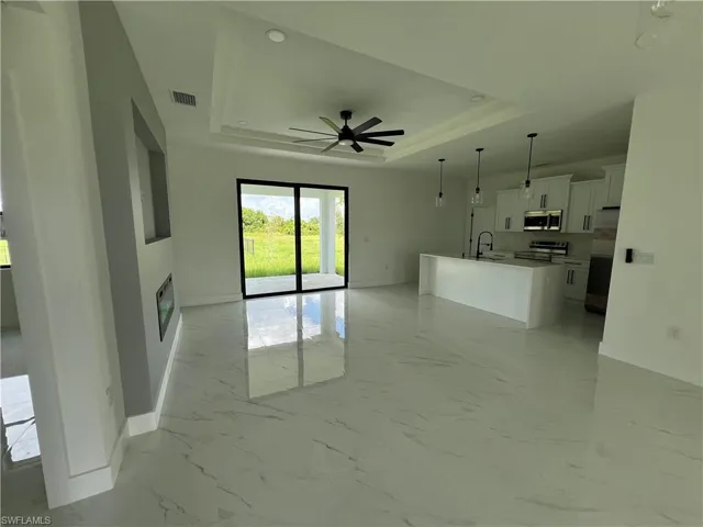 Unfurnished living room featuring light tile patterned floors, sink, ceiling fan, and a raised ceiling