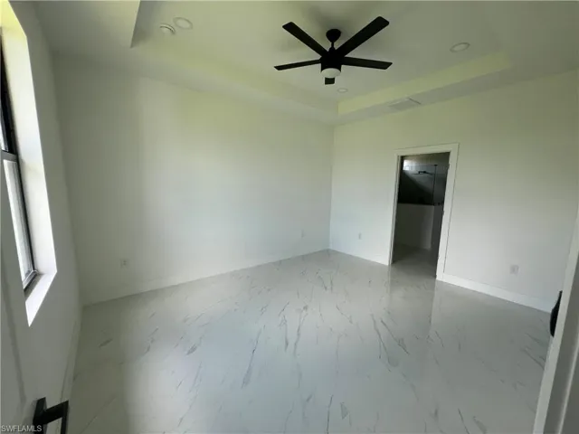 Tiled empty room featuring ceiling fan and a raised ceiling