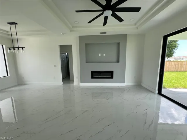 Unfurnished living room featuring a tray ceiling, light tile patterned floors, and ceiling fan
