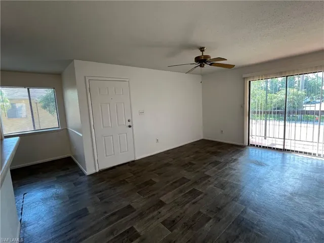 Empty room with ceiling fan, dark hardwood / wood-style floors, a healthy amount of sunlight, and a textured ceiling