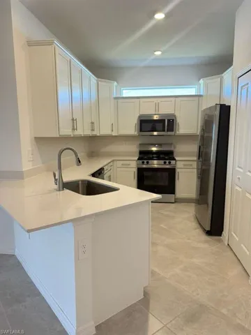 Kitchen featuring stainless steel appliances, white cabinetry, a peninsula, light stone countertops, and a breakfast bar area