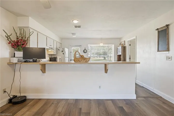 Kitchen featuring freestanding refrigerator, dark wood-style flooring, a kitchen bar, a peninsula, and baseboards