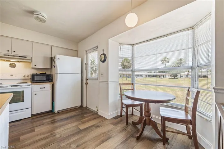 Kitchen featuring white appliances, under cabinet range hood, wood finished floors, light countertops, and white cabinetry