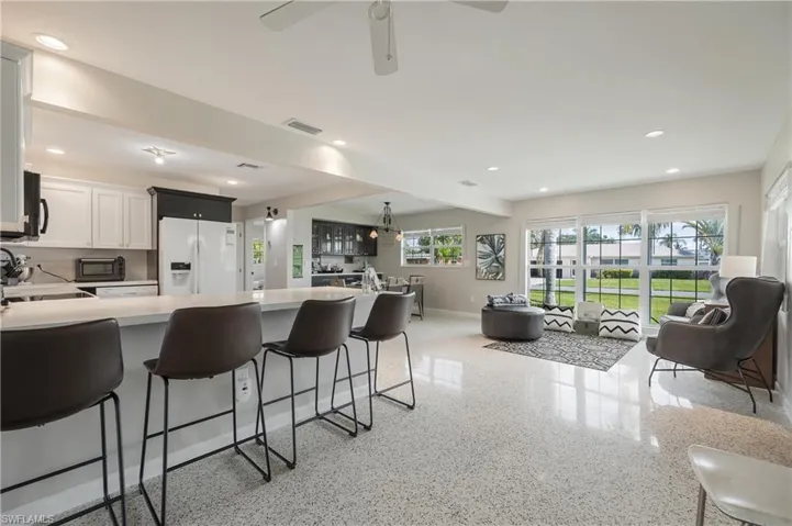 Kitchen featuring decorative backsplash, a kitchen bar, ceiling fan, white cabinets, and white refrigerator with ice dispenser