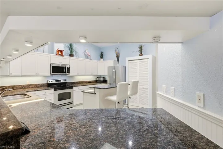 Kitchen featuring appliances with stainless steel finishes, dark stone countertops, a textured wall, white cabinets, and a wainscoted wall