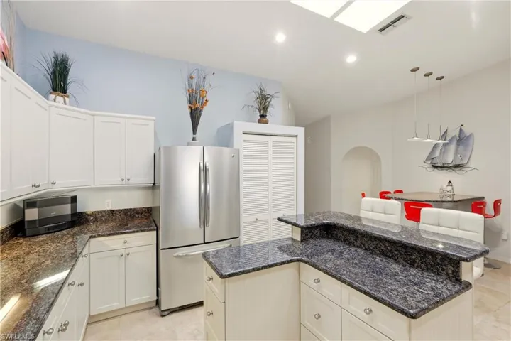 Kitchen with freestanding refrigerator, dark stone countertops, pendant lighting, light tile patterned floors, and white cabinets