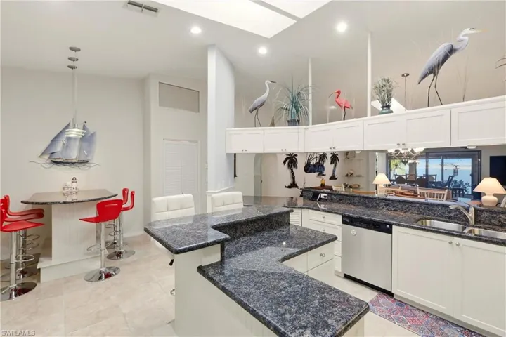 Kitchen featuring a towering ceiling, dark stone counters, dishwasher, white cabinets, and recessed lighting