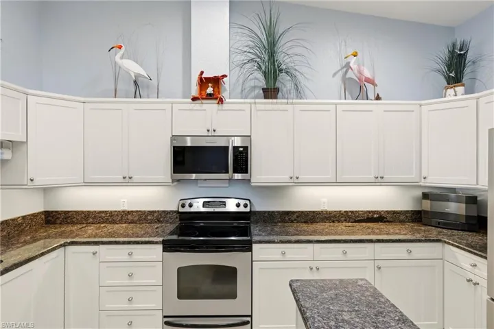 Kitchen featuring appliances with stainless steel finishes, white cabinetry, and dark stone counters