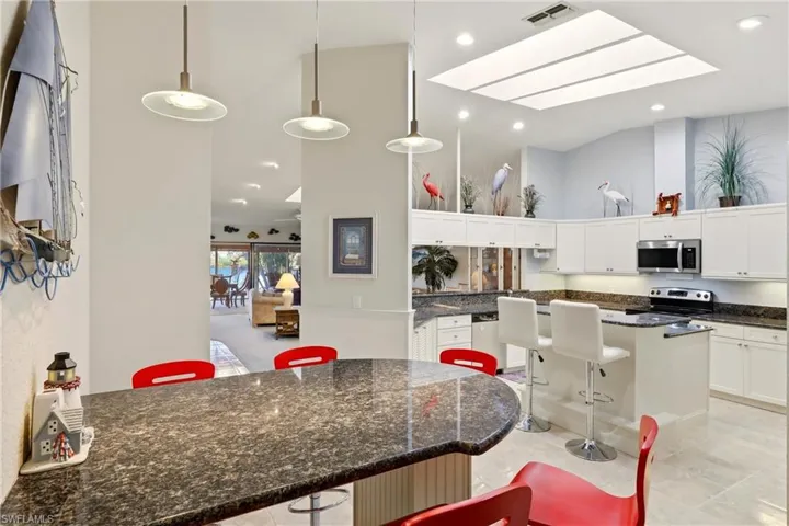 Kitchen with a breakfast bar, dark stone countertops, decorative light fixtures, white cabinetry, and high vaulted ceiling