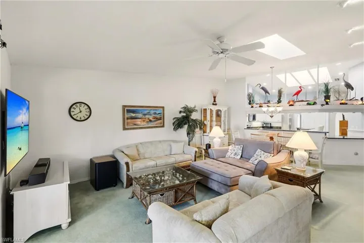 Living area with a ceiling fan, light colored carpet, and a skylight