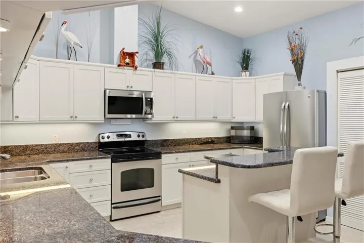 Kitchen with appliances with stainless steel finishes, white cabinetry, a kitchen bar, recessed lighting, and a high ceiling