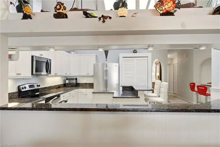 Kitchen featuring stainless steel appliances, dark stone counters, a high ceiling, white cabinets, and a peninsula