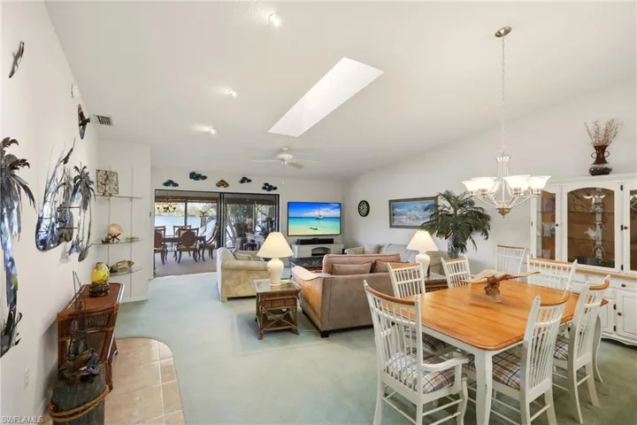Carpeted dining space featuring a skylight, a ceiling fan, a chandelier, and vaulted ceiling