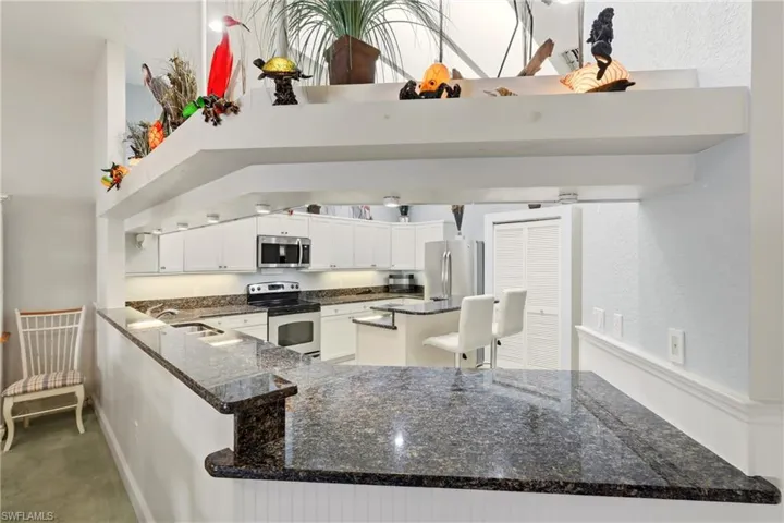 Kitchen featuring appliances with stainless steel finishes, dark stone counters, white cabinetry, a high ceiling, and a breakfast bar area