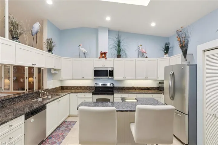 Kitchen with a high ceiling, stainless steel appliances, white cabinetry, a breakfast bar area, and a center island