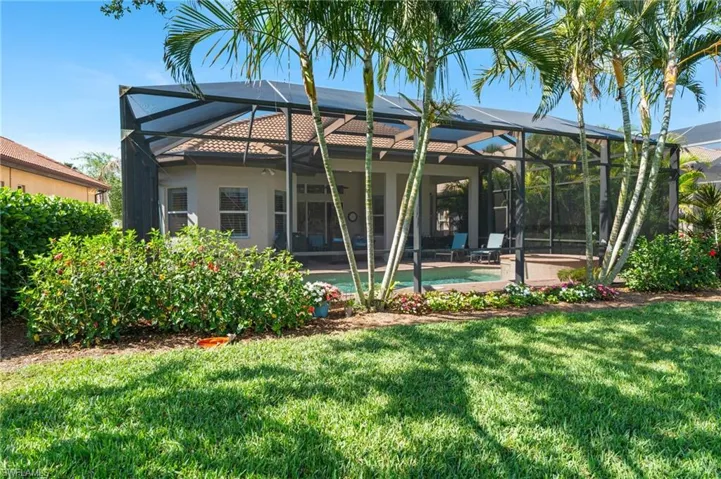 Rear view of property with glass enclosure, a lawn, stucco siding, and an outdoor pool