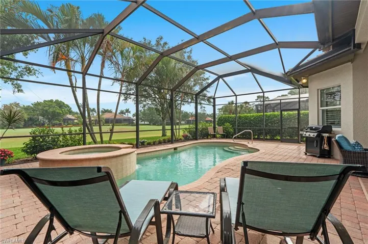 Pool featuring glass enclosure, a grill, a patio area, and an in ground hot tub