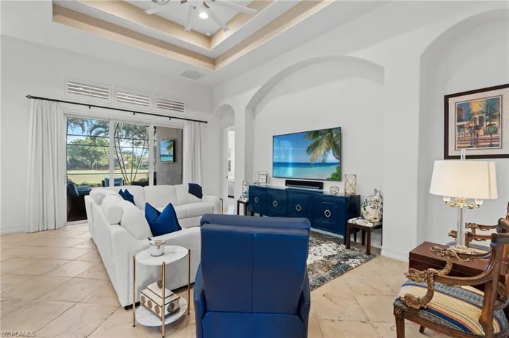 Living area with a raised ceiling, baseboards, visible vents, arched walkways, and ceiling fan