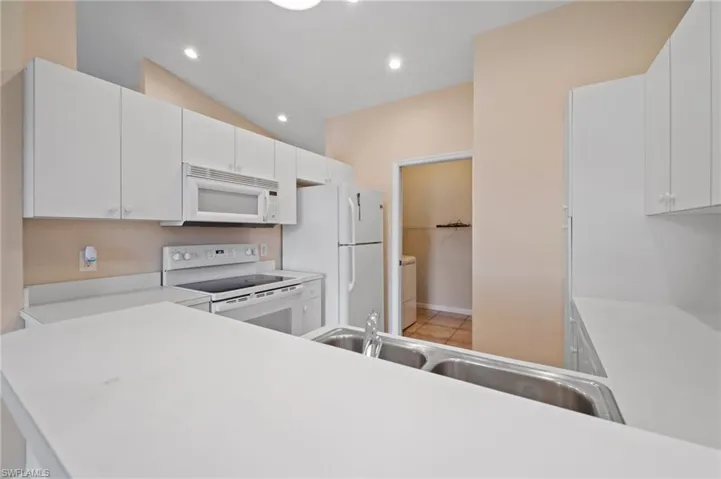Kitchen with white appliances, white cabinetry, lofted ceiling, and sink