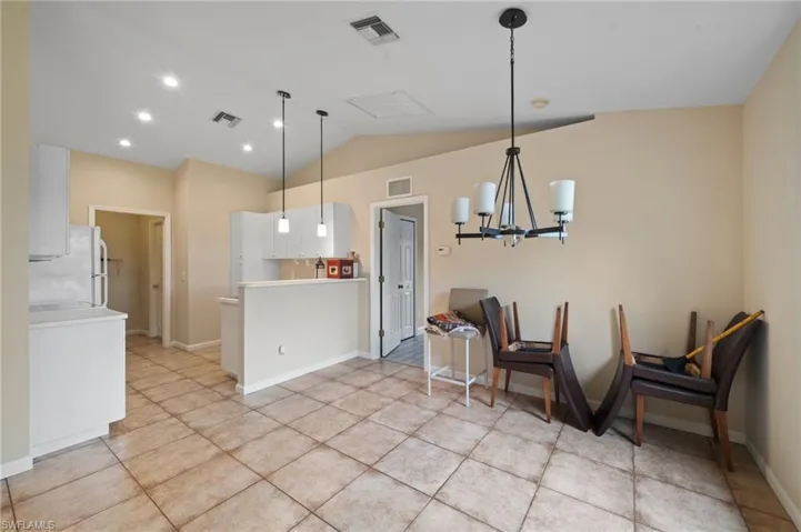 Kitchen featuring hanging light fixtures, white cabinetry, vaulted ceiling, a notable chandelier, and white refrigerator