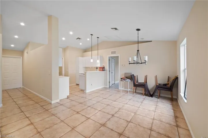 Kitchen featuring light tile patterned flooring, lofted ceiling, decorative light fixtures, white cabinets, and a notable chandelier