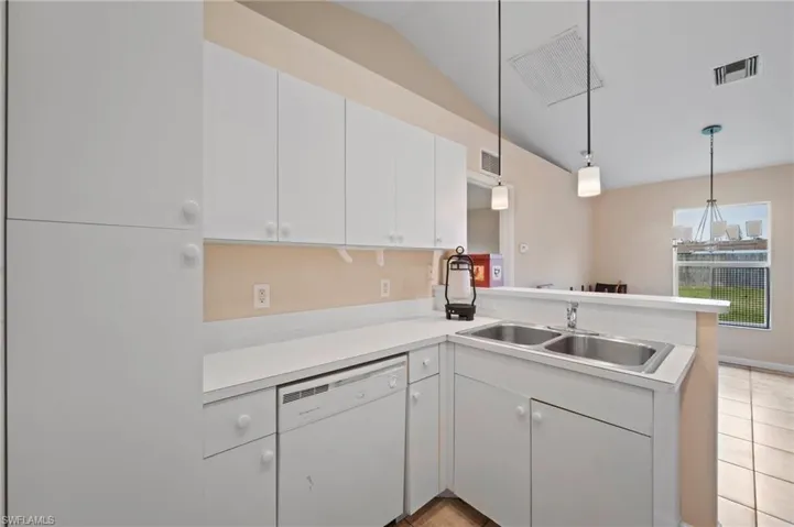 Kitchen with lofted ceiling, kitchen peninsula, white cabinetry, dishwasher, and sink