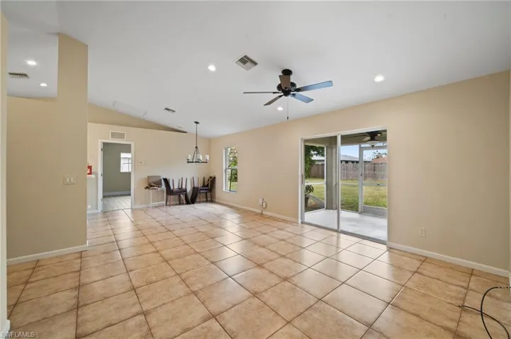 Unfurnished living room featuring vaulted ceiling, ceiling fan with notable chandelier, and light tile patterned floors
