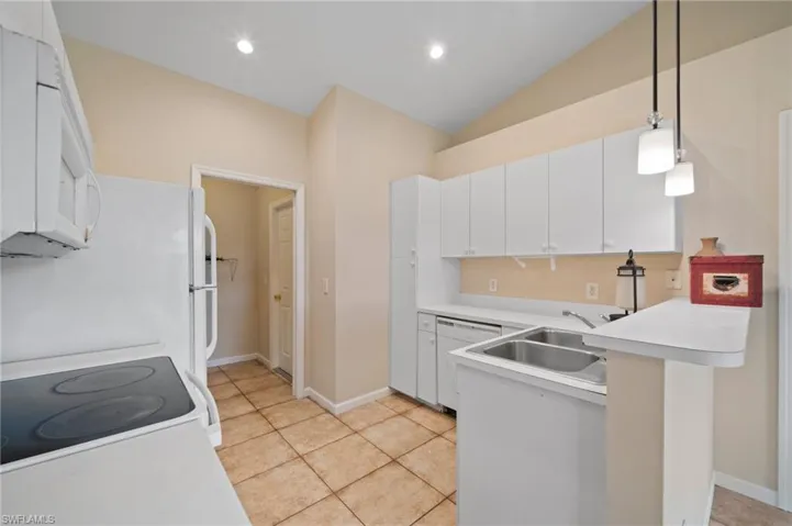 Kitchen with light tile patterned floors, white cabinetry, vaulted ceiling, pendant lighting, and white appliances