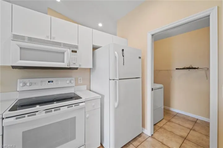 Kitchen featuring lofted ceiling, washer / clothes dryer, light tile patterned floors, white cabinetry, and white appliances