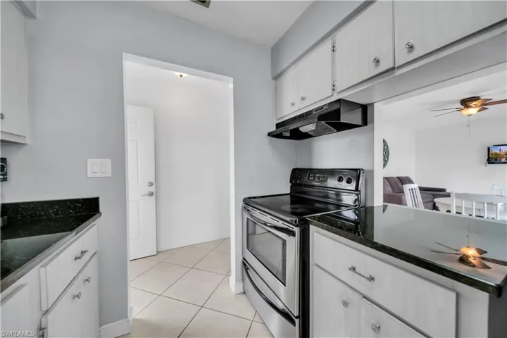 Kitchen with a ceiling fan, stainless steel range with electric cooktop, under cabinet range hood, dark stone countertops, and white cabinetry