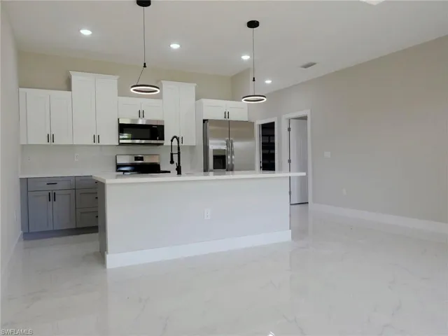 Modern kitchen featuring stainless steel appliances, white upper cabinetry, gray lower cabinetry, and a central island with a white countertop