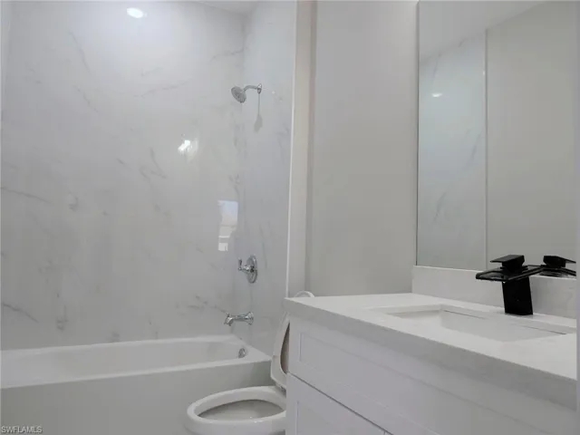 Bathtub with polished chrome fixtures, white tile surround, white vanity with integrated sink, light-toned countertop, and a black modern faucet