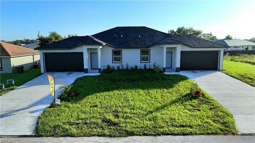 Duplex property featuring a dark shingled roof, light-colored exterior, attached garages, and a concrete driveway