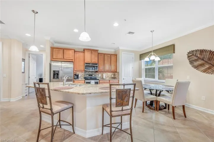Kitchen featuring appliances with stainless steel finishes, backsplash, sink, light stone countertops, and a breakfast bar
