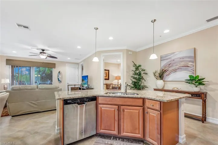 Kitchen with light tile patterned flooring, sink, stainless steel dishwasher, ceiling fan, and a center island with sink