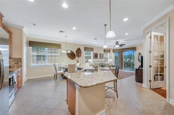 Kitchen featuring ceiling fan, decorative backsplash, sink, stainless steel range, and a center island with sink
