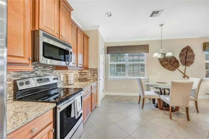 Kitchen featuring backsplash, appliances with stainless steel finishes, light stone countertops, a chandelier, and light tile patterned floors