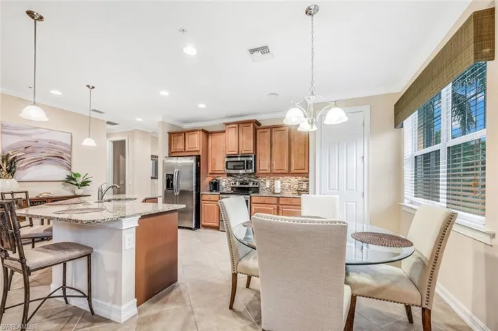 Kitchen featuring appliances with stainless steel finishes, light stone counters, an island with sink, tasteful backsplash, and light tile patterned floors