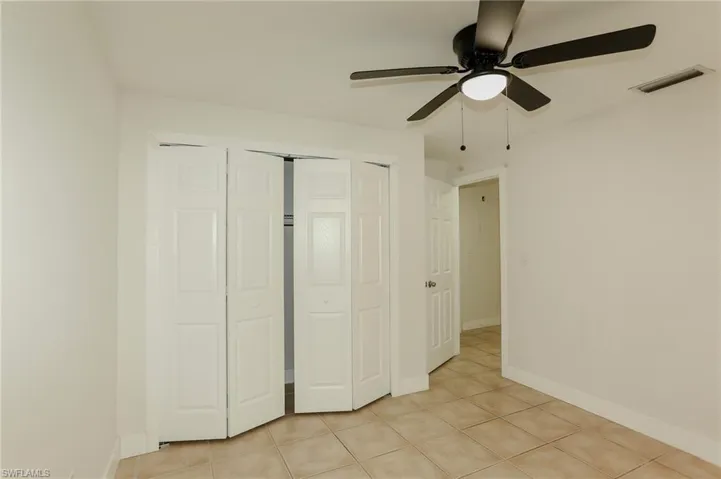 Interior room featuring neutral wall paint, tile flooring, a ceiling fan with integrated lighting, and bi-fold closet doors