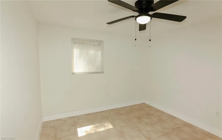 Spacious room featuring neutral-toned tile flooring, white walls, and a ceiling fan with integrated lighting