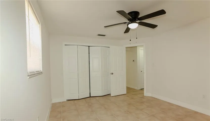 Room featuring neutral tone walls, tile flooring, a window with blinds, a ceiling fan, and bi-fold closet doors