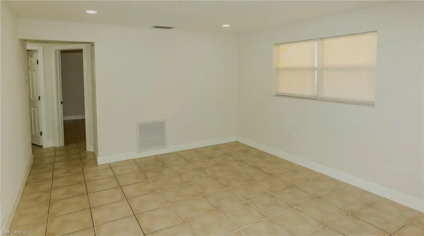 Spacious interior featuring neutral tile flooring, white baseboards, a window with horizontal blinds, recessed lighting, and a white interior door