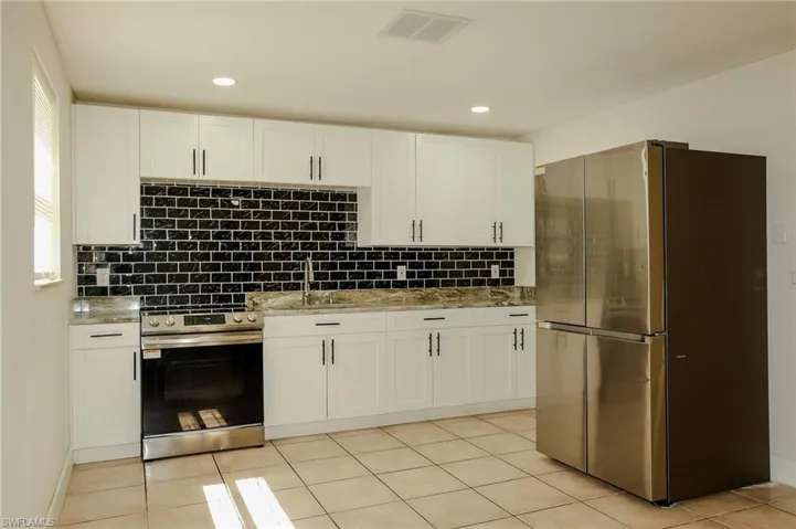 Kitchen featuring white shaker-style cabinetry, black subway tile backsplash, stone countertops, and stainless steel appliances