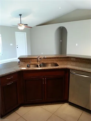 Kitchen with vaulted ceiling, light tile flooring, dishwasher, ceiling fan, and sink